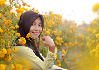 Portrait of smiling woman standing by yellow flowering plants