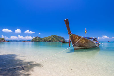 Boat moored on beach against blue sky