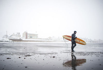 Surfer walks along maine beach during winter snow storm
