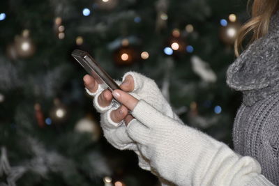 Midsection of woman using mobile phone while standing by christmas tree