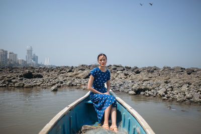 Portrait of smiling young woman standing on rock against sea