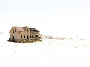 Abandoned building on snow covered land against clear sky