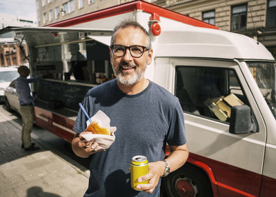 Portrait of happy male customer standing against food truck in city