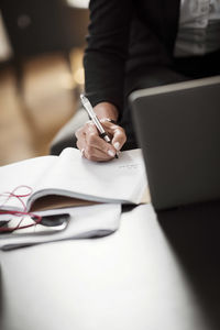 Midsection of businesswoman writing in book on table at hotel room