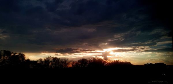 Silhouette trees against dramatic sky during sunset