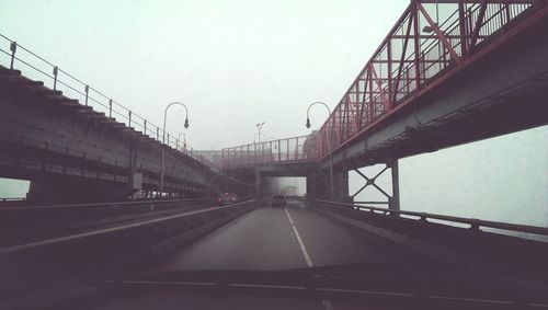 Low angle view of bridge seen through car windshield against sky during foggy weather