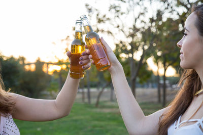 Cropped image of friends toasting beer bottles at park