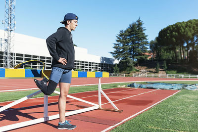 Side view of young athlete with prosthetic leg standing by railing on running track