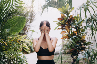 Young woman with hands in front of her face surrounded by lush tropical foliage