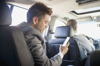 Young businessman looking at smartphone sitting in car service limousine