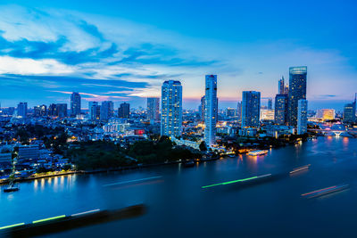 Illuminated buildings by river against sky in city