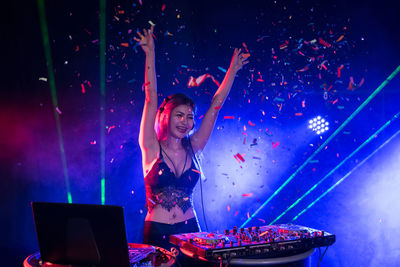 Cheerful female dj throwing confetti at concert