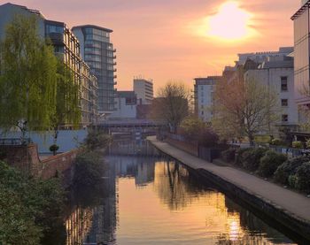 Buildings by river against sky during sunset