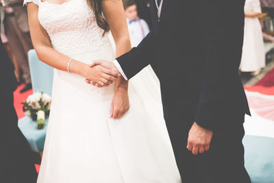 Midsection of couple holding hands during wedding ceremony
