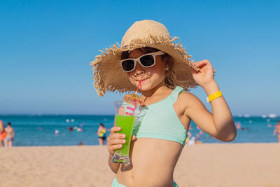 Young woman wearing sunglasses while standing at beach against sky