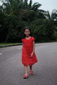 Portrait of cute girl wearing red dress while walking on road