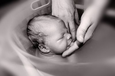 Cropped image of woman bathing baby in tub