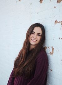 Portrait of smiling young woman standing against wall