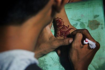 Midsection of man applying henna tattoo on woman hand