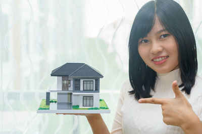 Portrait of smiling young woman pointing at model home