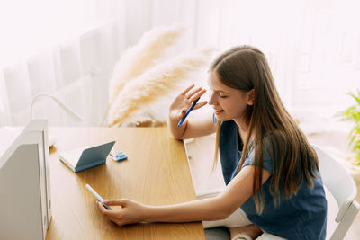 Young woman using mobile phone while sitting on bed at home