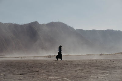 Woman walking on land against mountains and sky