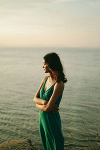 Side view of young woman looking at sea against sky during sunset