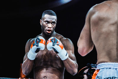 Portrait of shirtless man with arms raised against black background