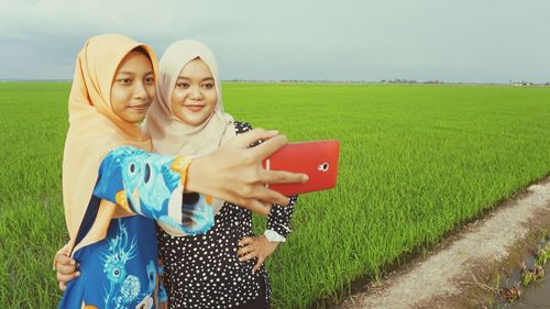 Smiling friends taking selfie on mobile phone at field