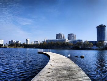 Jetty over river in city against blue sky