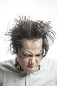 Close-up of frustrated man tossing hair against white background
