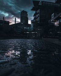 Surface level of wet street against buildings at dusk