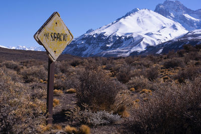Road sign on snow covered mountain against sky