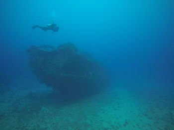 Scuba diver swimming near shipwreck in blue sea