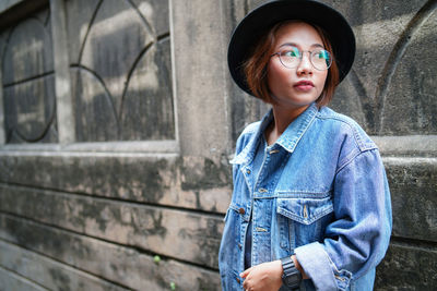 Young woman in hat standing against wall