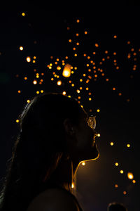 Low angle view of woman against illuminated lighting equipment at night