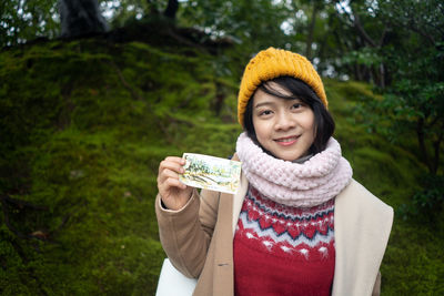 Portrait of smiling young woman showing paper while standing in forest