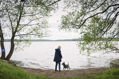 Rear view of senior woman standing with dog at lakeshore