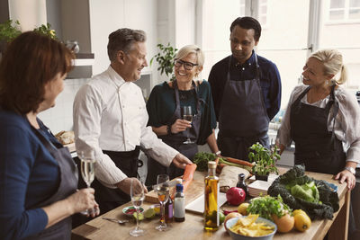 Happy chef preparing food while teaching to students standing at table