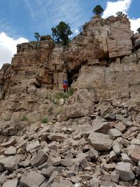 Low angle view of man climbing on rocky mountains against sky