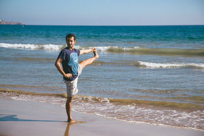 Man doing yoga on beach by sea against sky