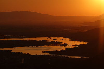 High angle view of silhouette city by sea against orange sky