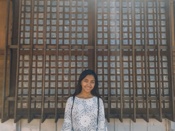 Portrait of a smiling young woman standing against window