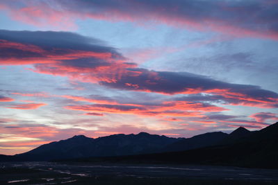 Scenic view of silhouette mountains against dramatic sky during sunset