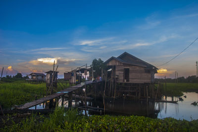 Houses by lake against sky during sunset