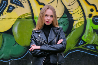 Portrait of young woman standing against graffiti wall