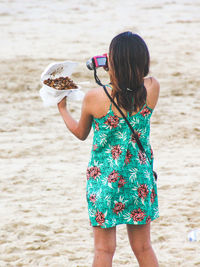 Rear view of woman photographing food at beach