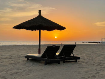 Chair on beach against sky during sunset