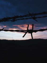 Silhouette of barbed wire against sky during sunset