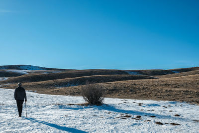 Rear view of man walking on snow covered landscape against clear blue sky